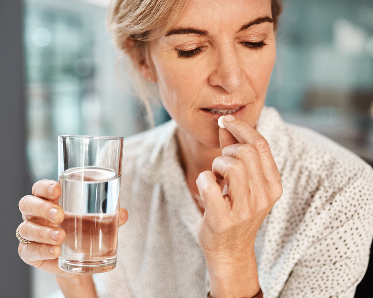 Ältere Frau nimmt Migräne Tabletten ein. In der anderen Hand hält sie ein Wasserglas hoch